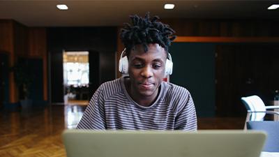 Student wearing headphones works on laptop.